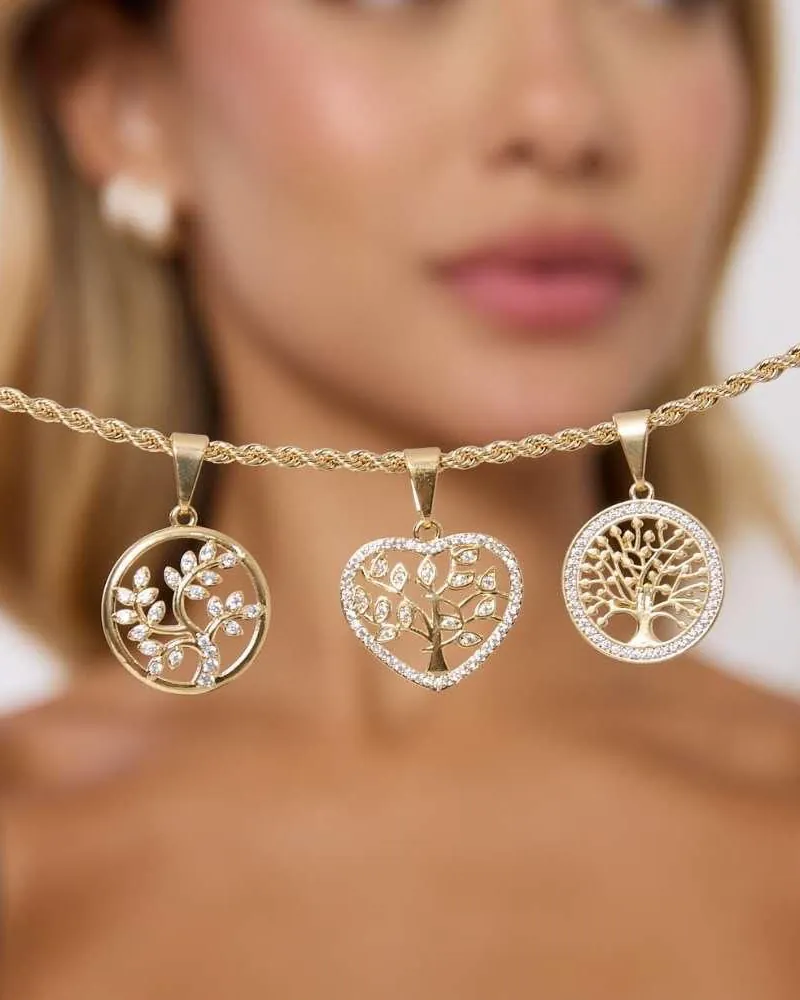 Três pingentes dourados de árvore da vida com zircônias, dois redondos e um de coração, num cordão dourado trançado, com a modelo desfocada atrás
